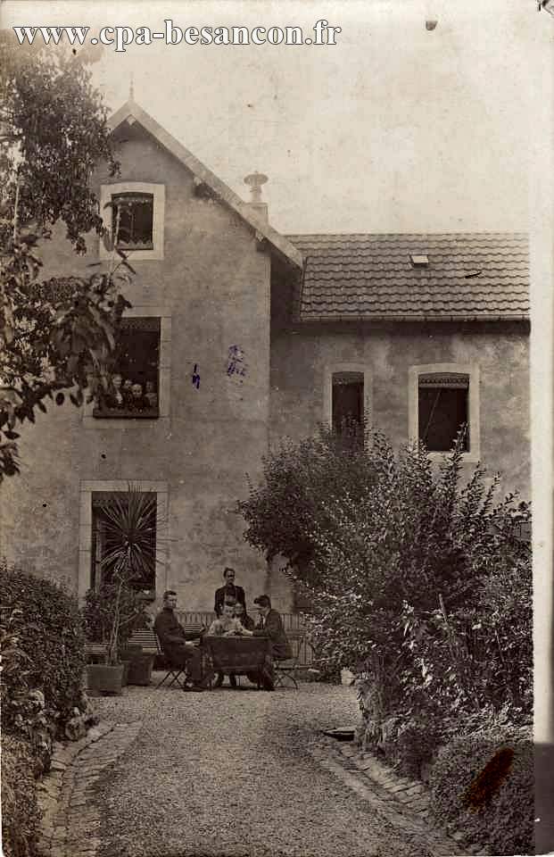Villa à identifier, avec personnes attablées dans le jardin et d'autres à une fenêtre.
